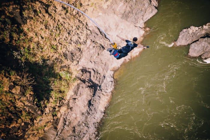 Man, with arms extended at shoulder height, free falls from the Victoria Falls Bridge