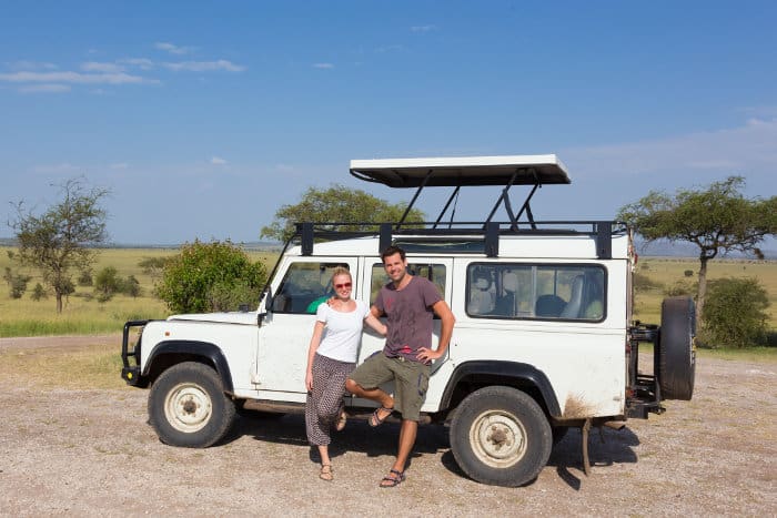 Couple on safari in Tanzania, posing in front of their four wheel drive