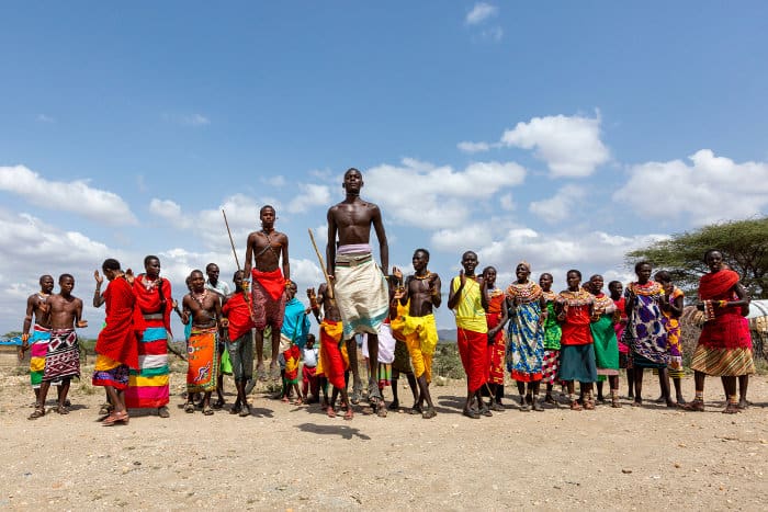A group of Samburu people, wearing brightly coloured traditional attire, perform a local dance